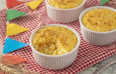 imagem mostra uma sobremesa cremosa de arroz doce de pamonha, em tom amarelo claro, decorada com canela e palha de milho.
