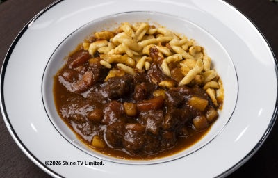 Goulash com molho escuro, carne cozida lentamente e spätzle salteado no prato branco